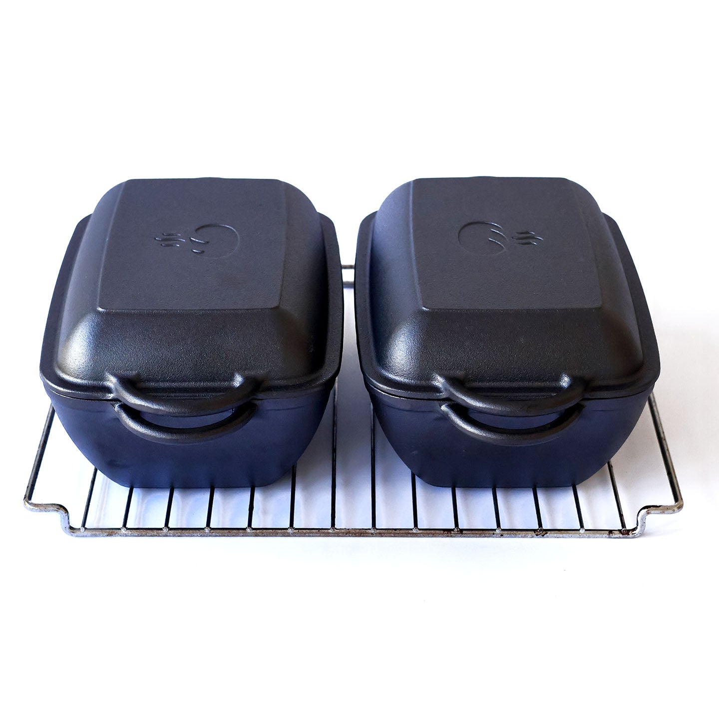 Two cast iron dutch ovens with lids on, side by side on an oven tray